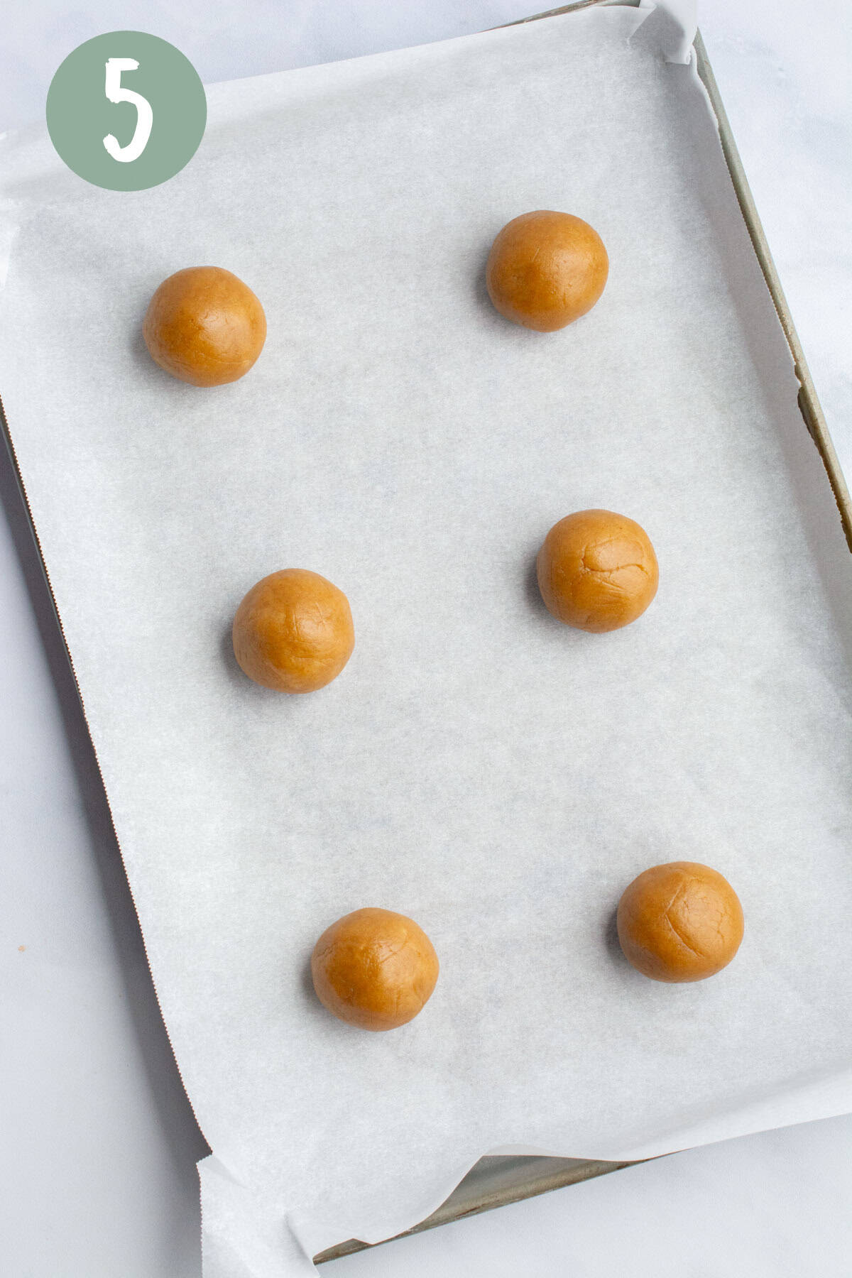 Balls of vegan peanut butter cookie dough on a baking sheet lined with parchment paper.