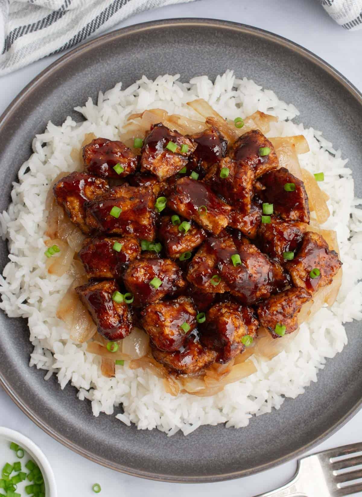 A plate of baked BBQ tofu with white rice and caramelized onions.