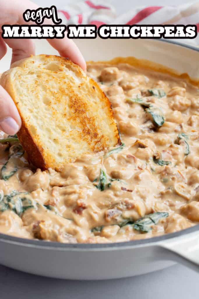 A hand dipping toasted bread into a pot of marry me chickpeas.