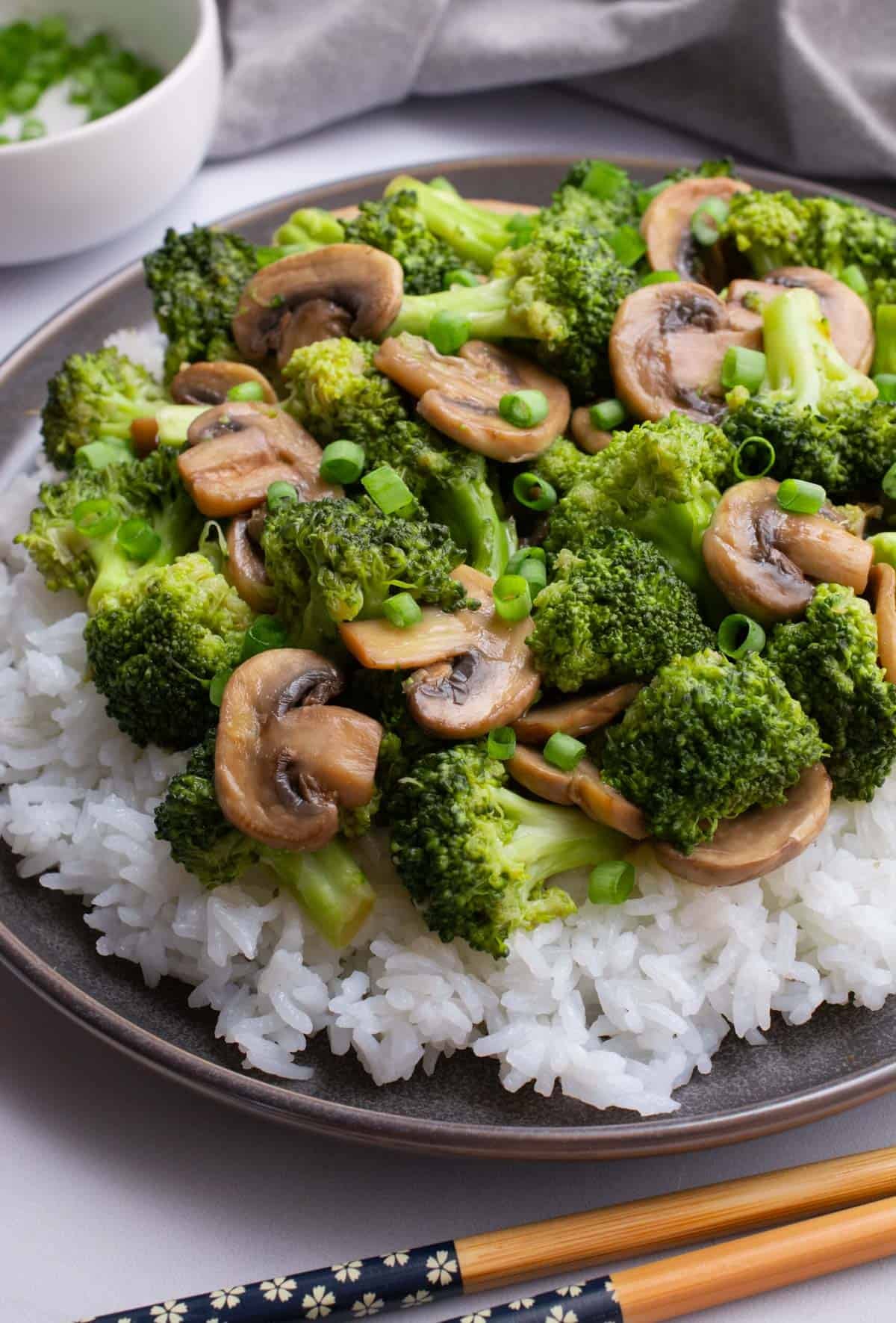 Plated mushroom broccoli stir-fry on a bed of white rice with chopsticks.
