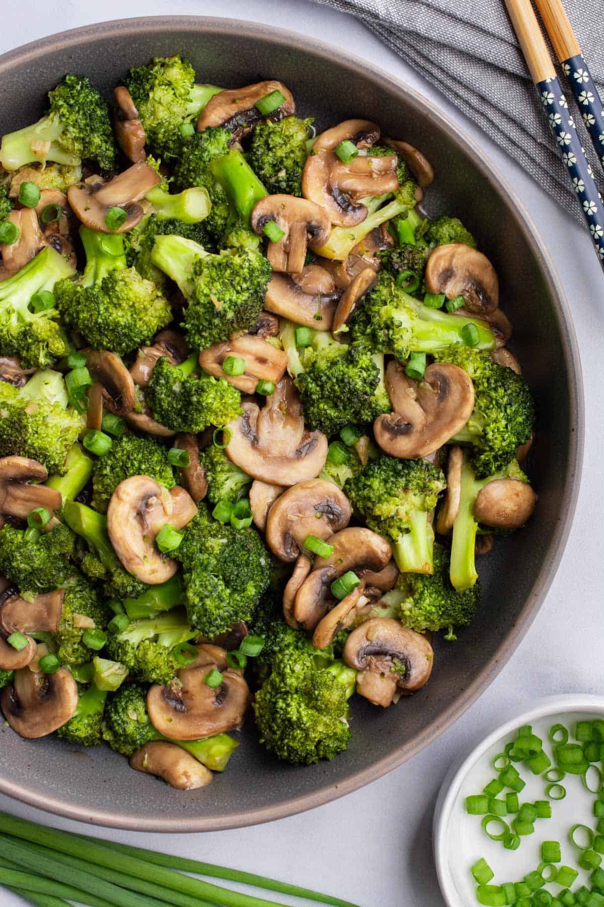 Mushroom and broccoli stir-fry topped with green onions in a serving bowl.