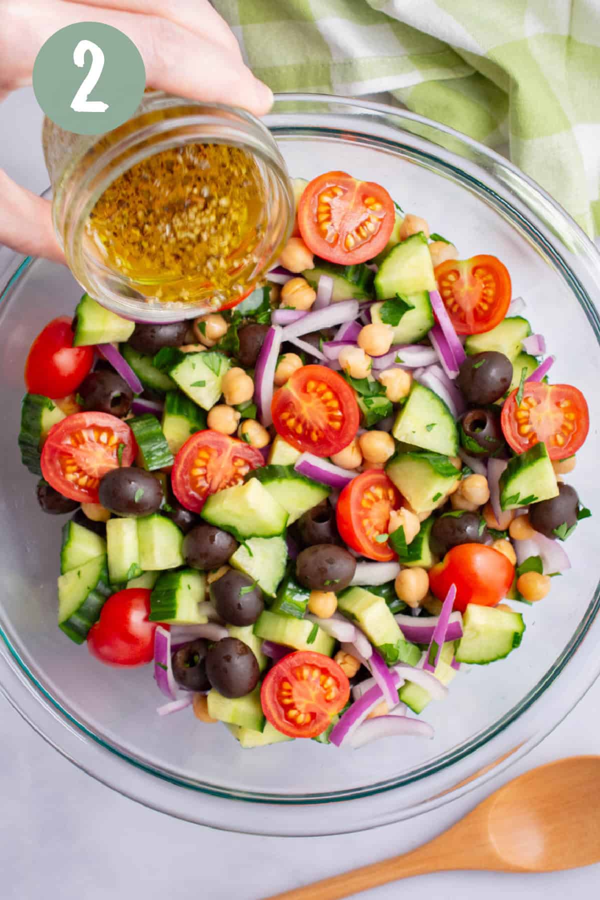 A hand pouring dressing over chopped cucumber salad.